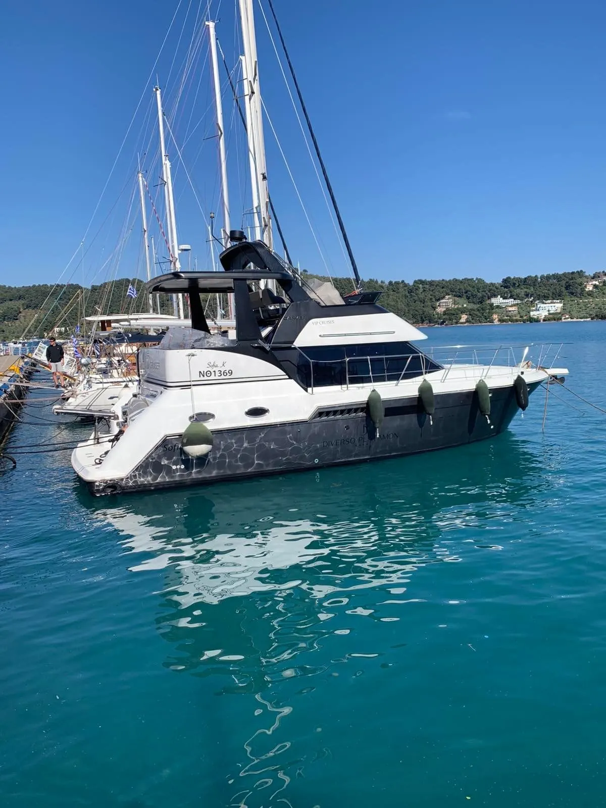 Sofia K moored alongside the quay, forested hills across the calm bay behind her